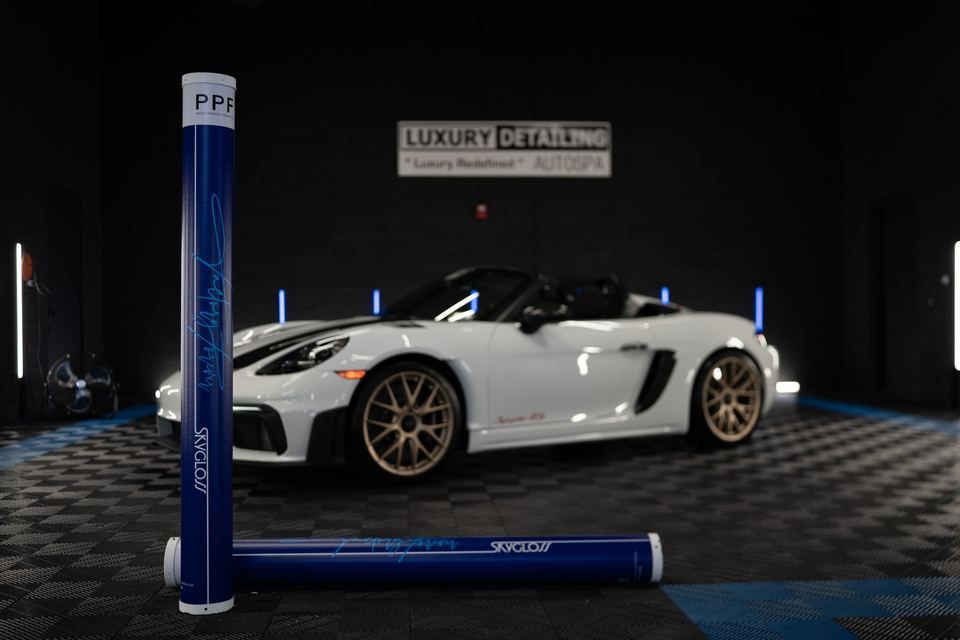 SkyGloss PPF rolls in front of a white Porsche in a detailing studio